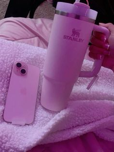 a pink phone case sitting next to a cup and coffee mug on a blanket with a woman's legs in the background