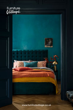 a bedroom with teal walls, orange and yellow bed linens and an upholstered headboard