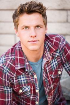 a young man wearing a plaid shirt poses for a photo