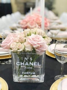 the table is set with pink roses and white flowers in a clear vase on it