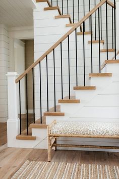 a bench sitting under a stair case next to a wooden bannister and white walls