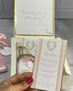 a hand holding a pink and gold wedding card in a box next to it's contents