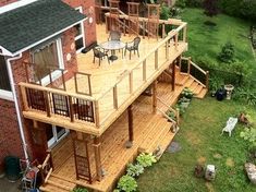 a large deck with chairs and tables in the middle of a garden area next to a brick building