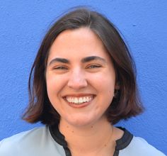 a woman smiling in front of a blue wall and wearing a black collared shirt