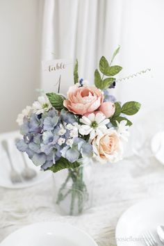 a vase filled with flowers sitting on top of a white table covered in plates and napkins