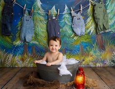 a baby sitting in a tub with clothes hanging on the clothes line above him and smiling at the camera