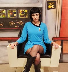 a woman in a blue shirt and black boots sitting on a chair with her legs crossed