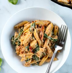 a white bowl filled with pasta and spinach on top of a marble countertop