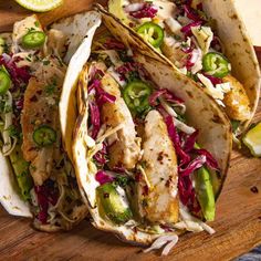 fish tacos with slaw, jalapenos and limes on a wooden platter