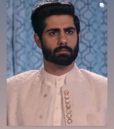 a man with a beard wearing a white shirt and pearls on his collar is looking at the camera