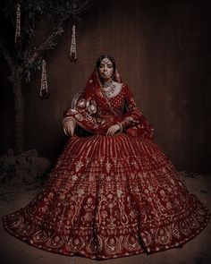 a woman in a red and white wedding dress sitting on a tree branch with beads hanging from it's branches