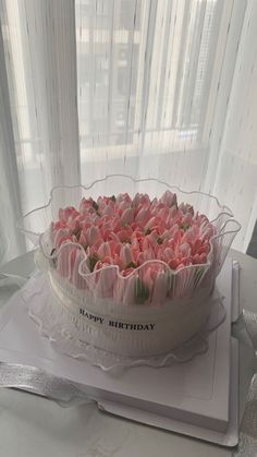 a birthday cake with pink flowers in a clear bowl on a table next to a window