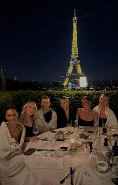 a group of women sitting at a table in front of the eiffel tower