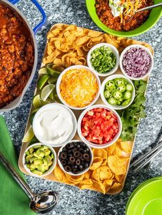 a platter filled with chili, cheese and tortilla chips next to two bowls of salsa