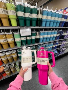 a person holding a pink and white coffee cup in front of a store shelf filled with different colored cups