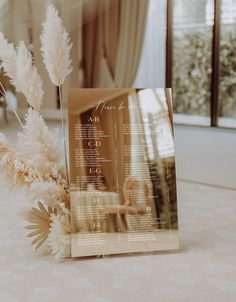 a close up of a menu on a table with flowers in the foreground and a mirror behind it