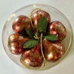 a glass bowl filled with shiny red and gold ornaments on top of a white table