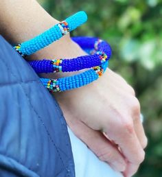 This bright handmade jewelry is fun to wear alone or in bunches. The set of bracelets features beads in multiple hues of blue and blue/green to add flair to any outfit. | This bright handmade jewelry is fun to wear alone or in bunches. The set of bracelets features beads in multiple hues of blue and blue/green to add flair to any outfit. Handmade by women artisans from the Maasai tribe in Kenya using traditional beading techniques passed down through the generations. Each color represents a spec Bohemian Blue Bracelets With Colorful Beads, Blue Bohemian Bracelets With Colorful Beads, Blue Bangle Jewelry With Large Beads, Blue Bohemian Beaded Bracelets With Large Beads, Blue Hand-strung Bracelets For Festival, Blue Bracelets With Colorful Beads For Festival, Festival Blue Bracelets With Colorful Beads, Bohemian Blue Beaded Bracelets With Tiny Beads, Blue Bohemian Beaded Bracelets With Tiny Beads