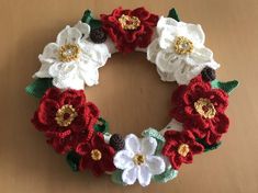 a crocheted wreath with white, red and green flowers sits on a table