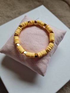 a yellow beaded bracelet sitting on top of a pink cushion next to a pillow