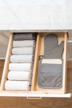 an open drawer with folded towels and other items in it on a wooden floor next to a marble counter top