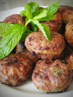 some meatballs are on a white plate with green leaves