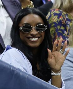 a woman wearing sunglasses and holding her hand up in the air at a tennis match