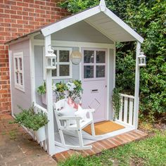 a white rocking chair sitting in front of a small shed with flowers on the porch