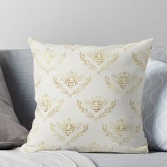 a white and gold throw pillow with a bee on it's back sitting on a couch