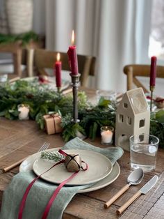 a table set for christmas dinner with candles and greenery on the dining room table