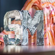 the letter m is made out of shiny silver mosaic tiles and sits on a table