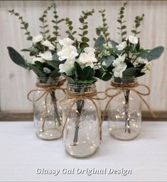 three mason jar vases with white flowers and greenery