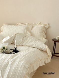 a bed with white comforter and pillows on it next to a small side table