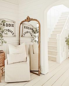 a living room with white walls and wooden flooring, two mirrors on the wall