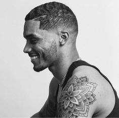 a black and white photo of a man with a flower tattoo on his arm smiling