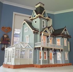 a doll house is displayed in front of a blue wall with white trim and windows