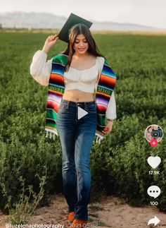 a woman walking through a field wearing jeans and a top with a graduation cap on her head