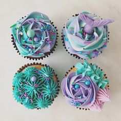 four cupcakes decorated with blue, purple and green icing on a white surface