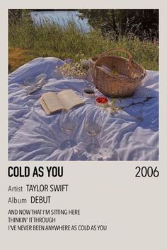 an open book sitting on top of a blanket next to a basket and wine glasses