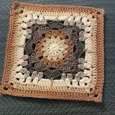 a crocheted square is sitting on the floor in front of a blue carpet