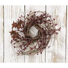 a wreath with red berries and star decorations on top of a white wooden background,