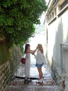 two women standing on the side of an alleyway touching each other's hands