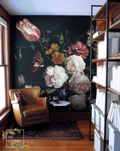 a room with a chair, bookshelf and flowers painted on the wall behind it