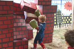 a little boy standing next to a giant red brick wall