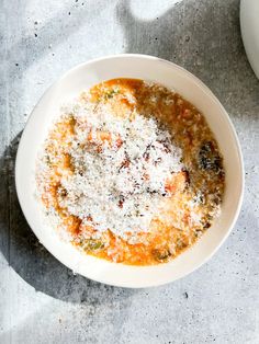 a white bowl filled with food sitting on top of a gray tablecloth next to a cup