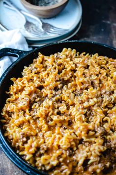 a skillet filled with macaroni and cheese on top of a wooden table