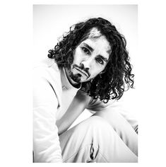 a black and white photo of a man with long curly hair sitting on the ground