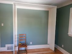 an empty room with blue walls and wooden flooring in the foreground is a chair