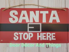 a red santa sign hanging on the side of a wooden wall that says, stop here door decor and things