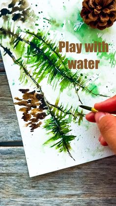 a person is holding a pine cone and painting on paper with watercolors in front of them